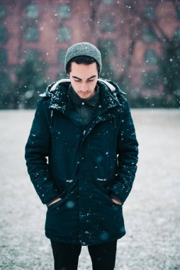 Genç adam kar yağarken parkta duruyor.