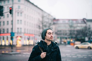 Genç adam kar yağarken sokakta duruyor.