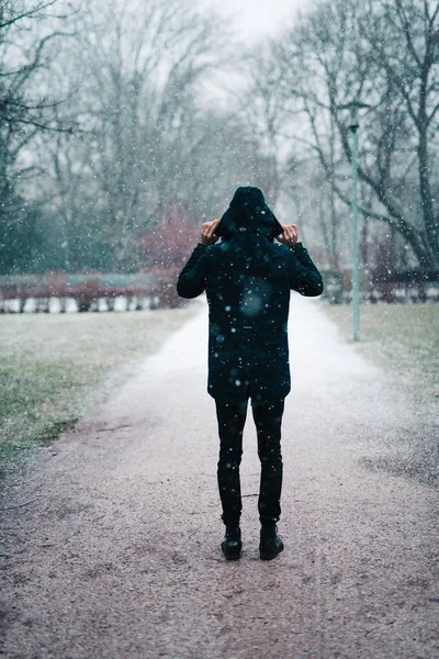 Young man standing in park while snowing — Stock Photo, Image