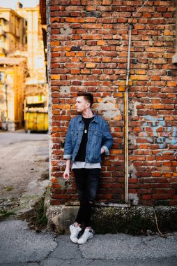 Duvarın önünde elinde sigara tutan genç bir adam.