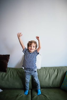 Kanepede kollarını kaldırmış küçük bir çocuk.