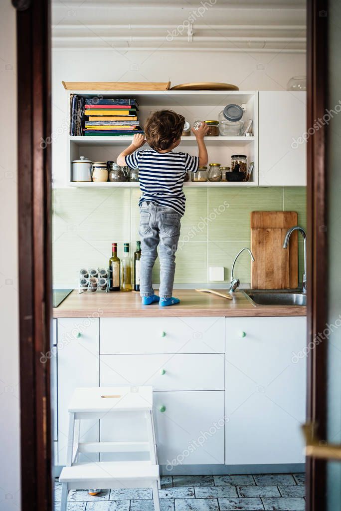 Little boy standing on a countertop in his kitchen