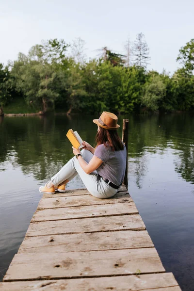 Νεαρή Γυναίκα Στην Προβλήτα Του Ποταμού Διαβάζοντας Βιβλίο — Φωτογραφία Αρχείου