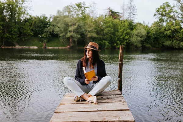 Νεαρή Γυναίκα Στην Προβλήτα Του Ποταμού Διαβάζοντας Βιβλίο — Φωτογραφία Αρχείου