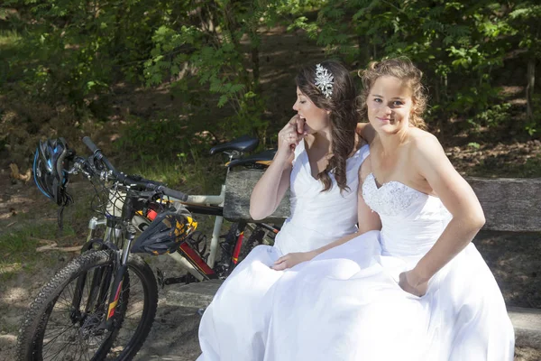 Deux mariées posent sur un banc en bois en forêt avec des vélos de montagne ne — Photo