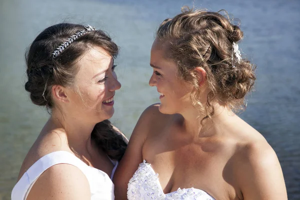 Apenas casado feliz casal lésbico em vestido branco perto de pequeno lago — Fotografia de Stock