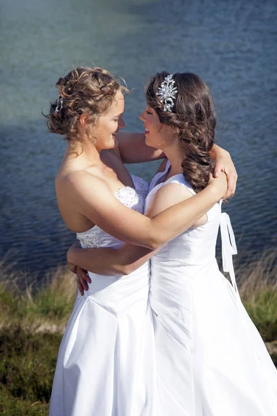 Apenas casado feliz casal lésbico em vestido branco perto de pequeno lago — Fotografia de Stock