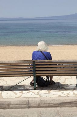 yaşlı Bayan yalnız bankta oturur ve Yunanistan Deniz bakar