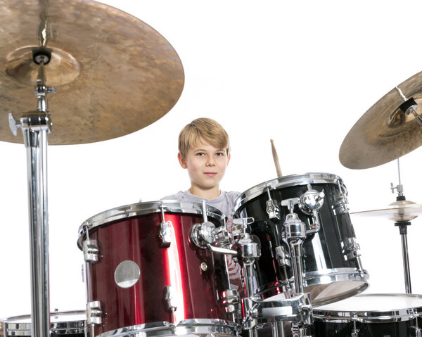 мальчик-подросток играет на барабанах в студии против белой спинки
