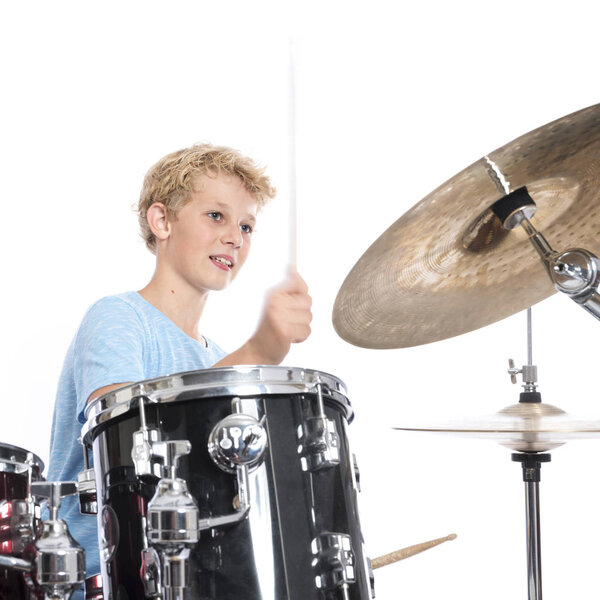 blond teen boy plays drums at drumkit in studio against white ba