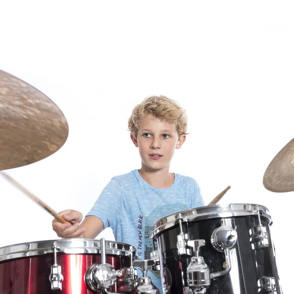 blond teen boy plays drums at drumkit in studio against white ba