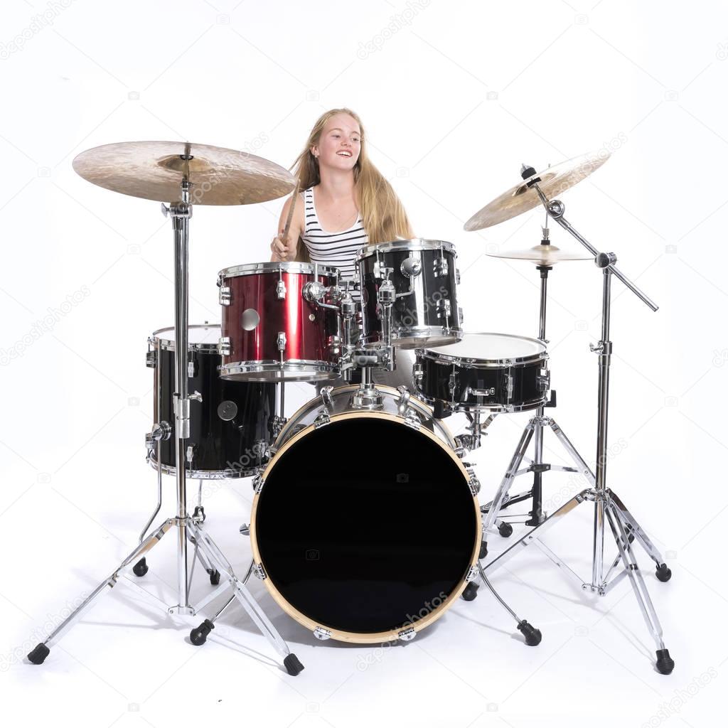 young blond teenage girl plays the drums in studio against white