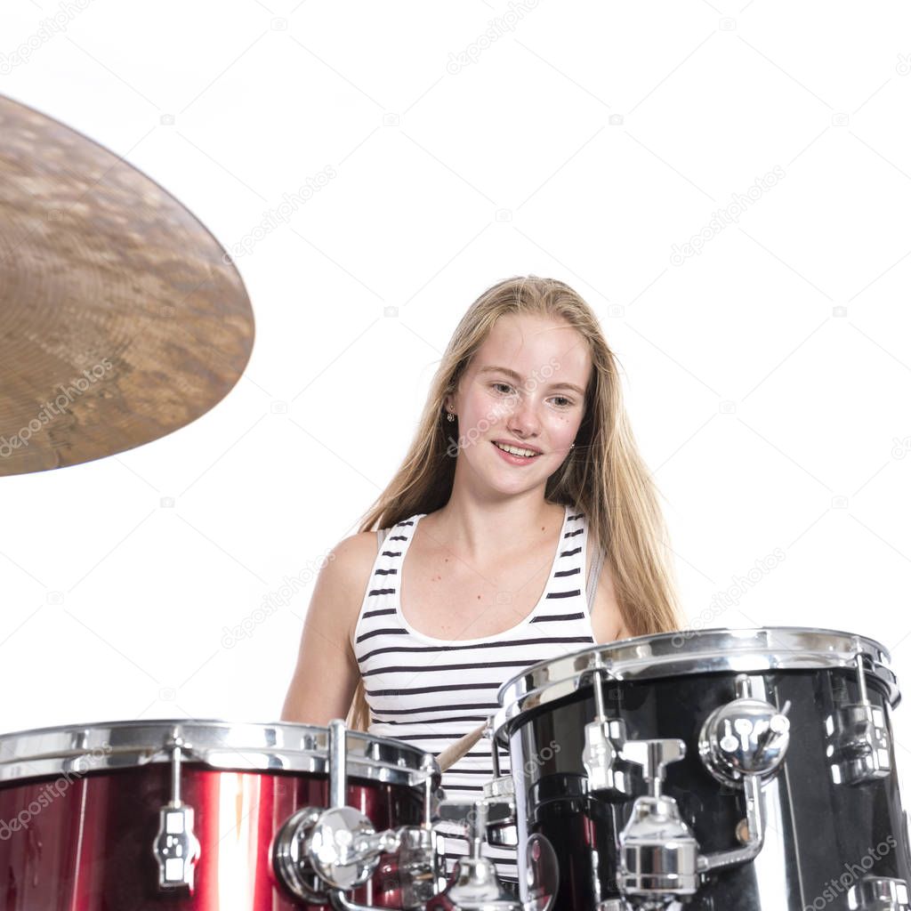 young blond teenage girl plays the drums in studio against white