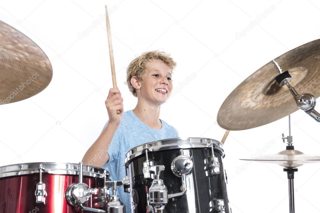 blond teen boy plays drums at drumkit in studio against white ba