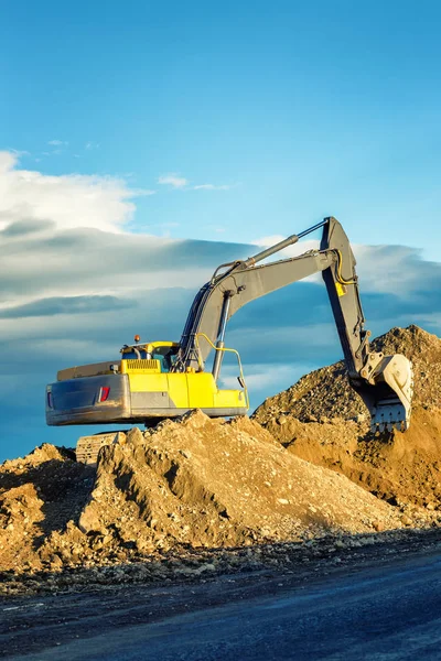 Excavator on a sand hill against a beautiful blue sky and mounta