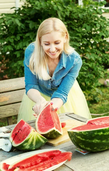 Beautiful girl cuts a watermelon in the garden — Stock Photo, Image