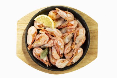 Tahta bir tahtanın üzerinde porsiyonlu demir tavada limonlu karidesler. Beyaz arkaplan üzerinde izole edilmiş.