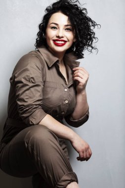Genç, gülen kadın. Parlak esmer, gri arka planda kıvırcık saçlı.. 