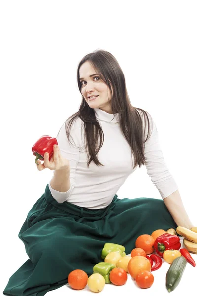 A young smiling female vegetarian is sitting next to a variety of vegetables and fruits. Isolated over white background. — Stock Photo, Image