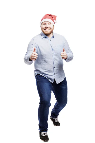 Hombre pelirrojo sonriente con barba en sombrero de Santa Claus, vaqueros y una camisa azul. A toda altura. Aislado sobre fondo blanco . — Foto de Stock