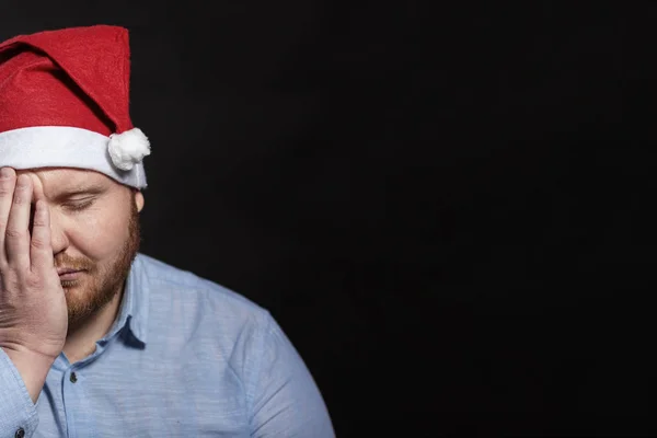 Um homem triste com uma barba vermelha em um chapéu de Papai Noel cobriu seu rosto — Fotografia de Stock