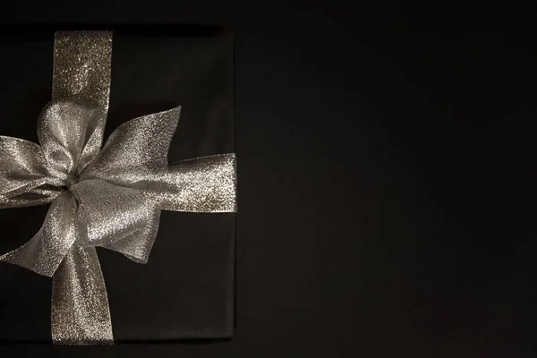 Black gift box with a silver  bow on a black background. Card. Space for text.