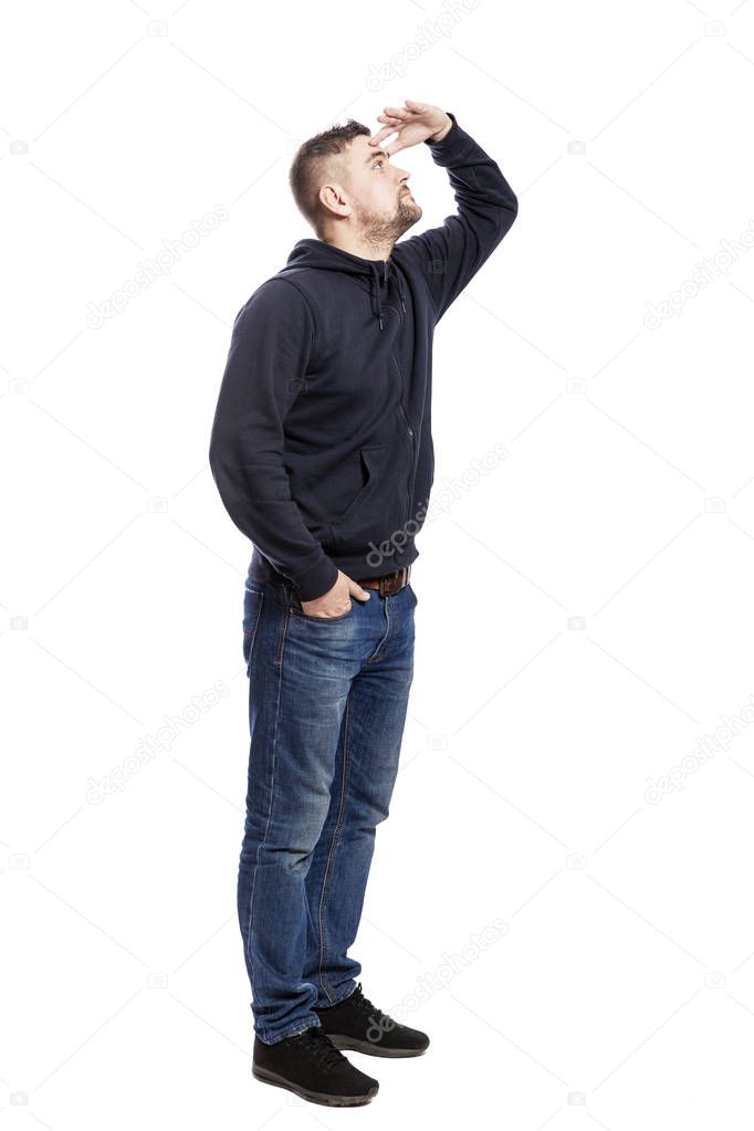 A handsome young man in jeans stands and looks into the distance. Hands in pockets. Side view. Isolated over white background. 