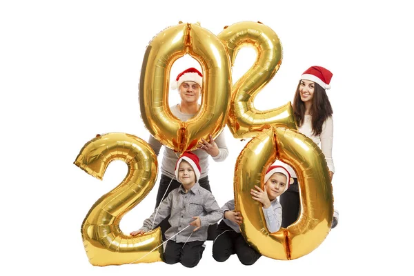 Happy family in caps of Santa Claus holds inflatable golden balloons in the form of numbers 2020. Festive mood. Isolated over white background. — Stock Photo, Image