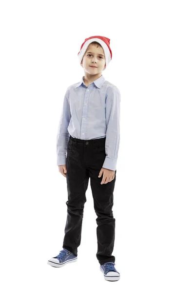 Noel Baba şapkalı şirin bir okul çocuğu ayakta duruyor. Tam yükseklik. Beyaz arkaplan üzerinde izole edilmiş. — Stok fotoğraf