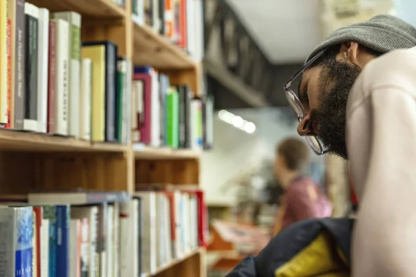 En ung man väljer en bok på en hylla i en butik. Utbildning och hobbyer. Närbild. — Stockfoto