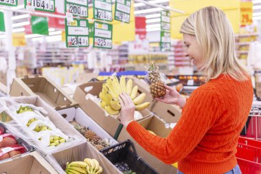 Gülümseyen genç kadın süpermarkette muz topluyor. Vejetaryenlik ve sağlıklı beslenme.
