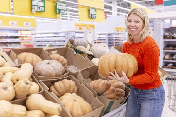Jovem sorridente com uma grande abóbora num supermercado. Vegetarianismo e alimentação saudável . — Fotografia de Stock