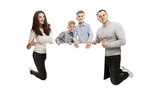 Jonge glimlachende familie met twee kinderen heeft een leeg spandoek. Geïsoleerd over witte achtergrond. Ruimte voor tekst. — Stockfoto