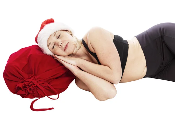 Eine junge Frau mit Weihnachtsmannmütze schläft auf einem Sack mit Geschenken. Ferienmärchen. isoliert über weißem Hintergrund. — Stockfoto