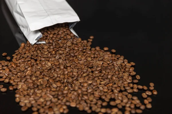 Packing with grains of coffee on a black background. Close-up. Space for text.