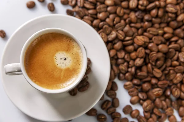 Una piccola tazza di caffè bianco sta su chicchi di caffè. Piacere profumato. Spazio per il testo. Fondo bianco . — Foto Stock