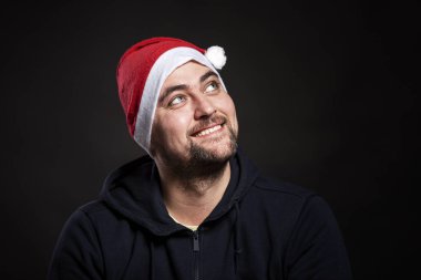 Noel Baba şapkalı gülümseyen yakışıklı genç adam yukarı bakıyor. Siyah arka plan. Yakın plan..