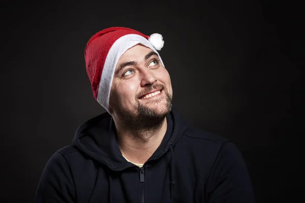 Sonriente joven guapo con sombrero de Santa Claus mira hacia arriba. Fondo negro. Primer plano . —  Fotos de Stock