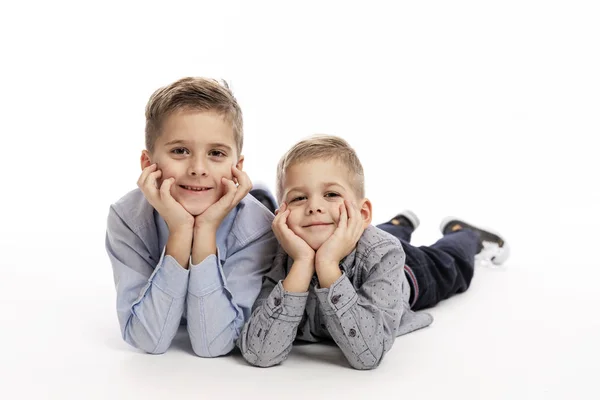 Dos hermanos con camisas azules yacen apoyando sus cabezas en sus manos y sonriendo. Fondo blanco . — Foto de Stock