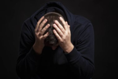 Kafası elinde oturan bir adam var. Depresyon ve umutsuzluk. Bulanık. Siyah arka plan. Yakın plan..