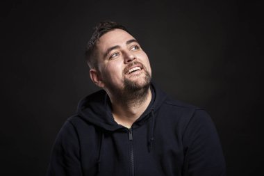 Sakallı, güzel, genç, esmer bir adam başını kaldırıp gülüyor. Yakın plan. Siyah arkaplan.