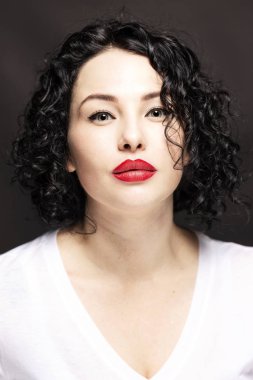 Beyaz tişörtlü güzel, ciddi, genç bir kadın. Kıvırcık saçlı, parlak esmer. Siyah arka plan. Yakın plan.. 