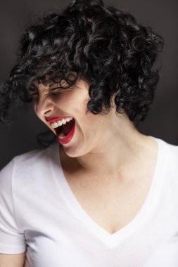 Beyaz tişörtlü güzel genç bayan gülüyor. Kıvırcık saçlı, parlak esmer. Siyah arka plan. Yakın plan.. 