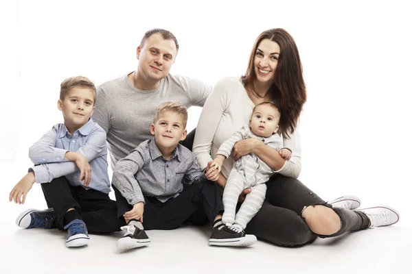 Een jong gezin met drie kinderen knuffelt en glimlacht terwijl ze zitten. Ze kijken naar de camera. Liefde en tederheid. Witte achtergrond. — Stockfoto