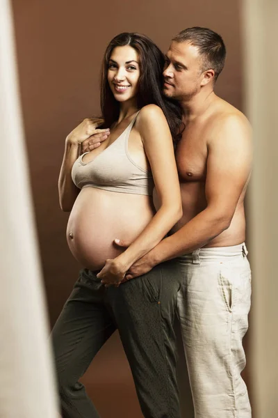 Genç, hamile, esmer bir kadın çıplak bir adama sarılıyor. Doğumu ve şefkati bekliyorum.. — Stok fotoğraf