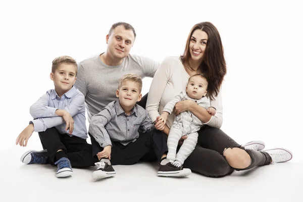 Una familia joven con tres hijos se abraza y sonríe mientras está sentada. Miran a la cámara. Amor y ternura. Fondo blanco . —  Fotos de Stock