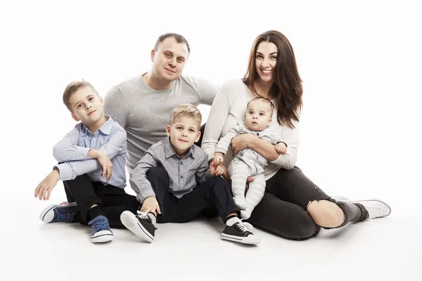 Una giovane famiglia con tre bambini abbracci e sorrisi seduti. Guardano la telecamera. Amore e tenerezza. Fondo bianco . — Foto Stock