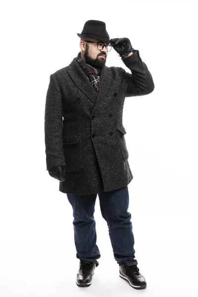 Elegante hombre con barba en abrigo y sombrero. Él está en pleno crecimiento sobre un fondo blanco y se aferra a su sombrero . — Foto de Stock