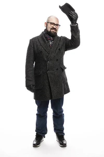 Un homme élégant avec une barbe dans un manteau et un chapeau. Il se tient en pleine croissance sur fond blanc et s'accroche à son chapeau . — Photo