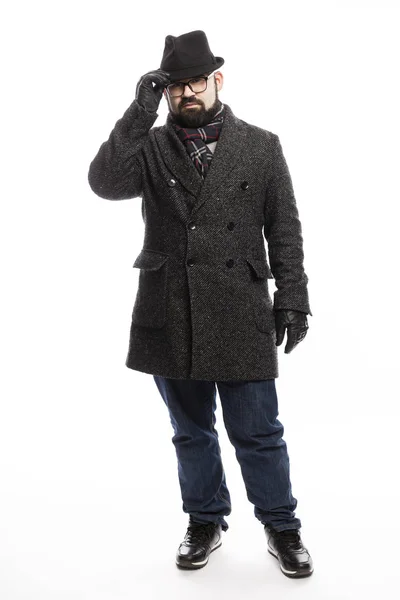 Elegante hombre con barba en abrigo y sombrero. Él está en pleno crecimiento sobre un fondo blanco y se aferra a su sombrero . — Foto de Stock